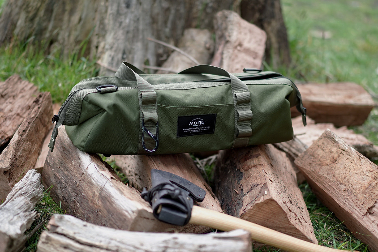 Mogu outdoors Utility tool bag sitting on top of a pile of firewood looking stylish with designed label and an axe in the foreground
