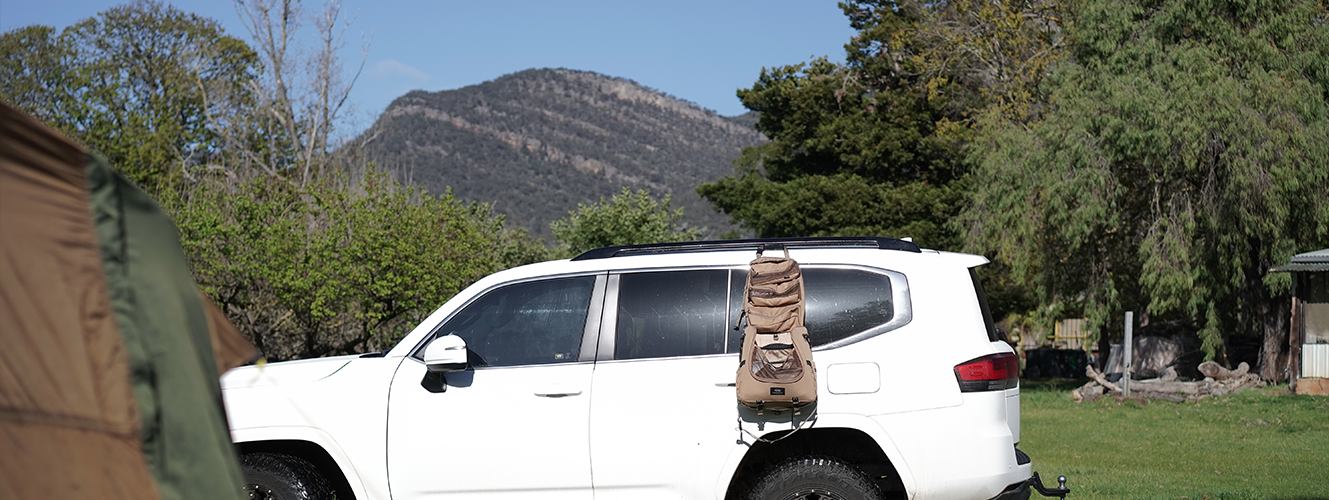 Underneath the background of a Grampians mountain peak, a car is parked on a campground with a camel colored kitchen caddy hanging from the side of the car, open and ready for camp cooking